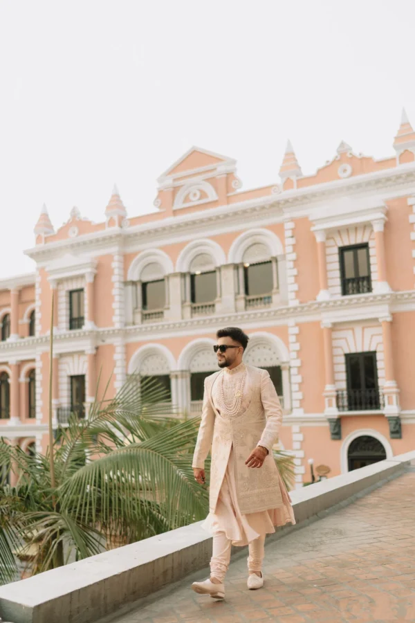 3. A groom dressed in an embellished ivory sherwani and multi-layered pearl necklaces walks along an outdoor stone terrace at Hotel Yak & Yeti in Kathmandu, Nepal.
