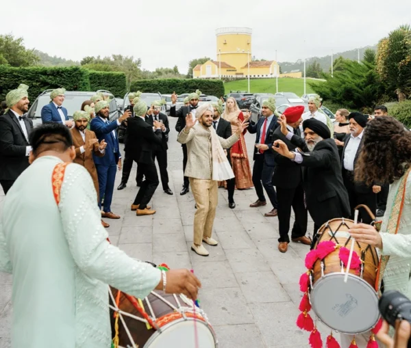 A groom dances during his outdoor baraat procession surrounded by guests in green turbans and traditional dhol players at Penha Longa Resort in Sintra, Portugal.