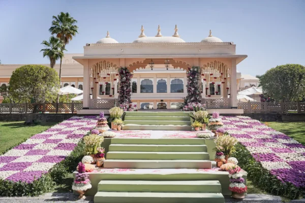 A wide stone staircase flanked by a checkered white and purple floral carpet leads to a traditional arched pavilion mandap decorated with flower pillars at Trident Hotel Udaipur.
