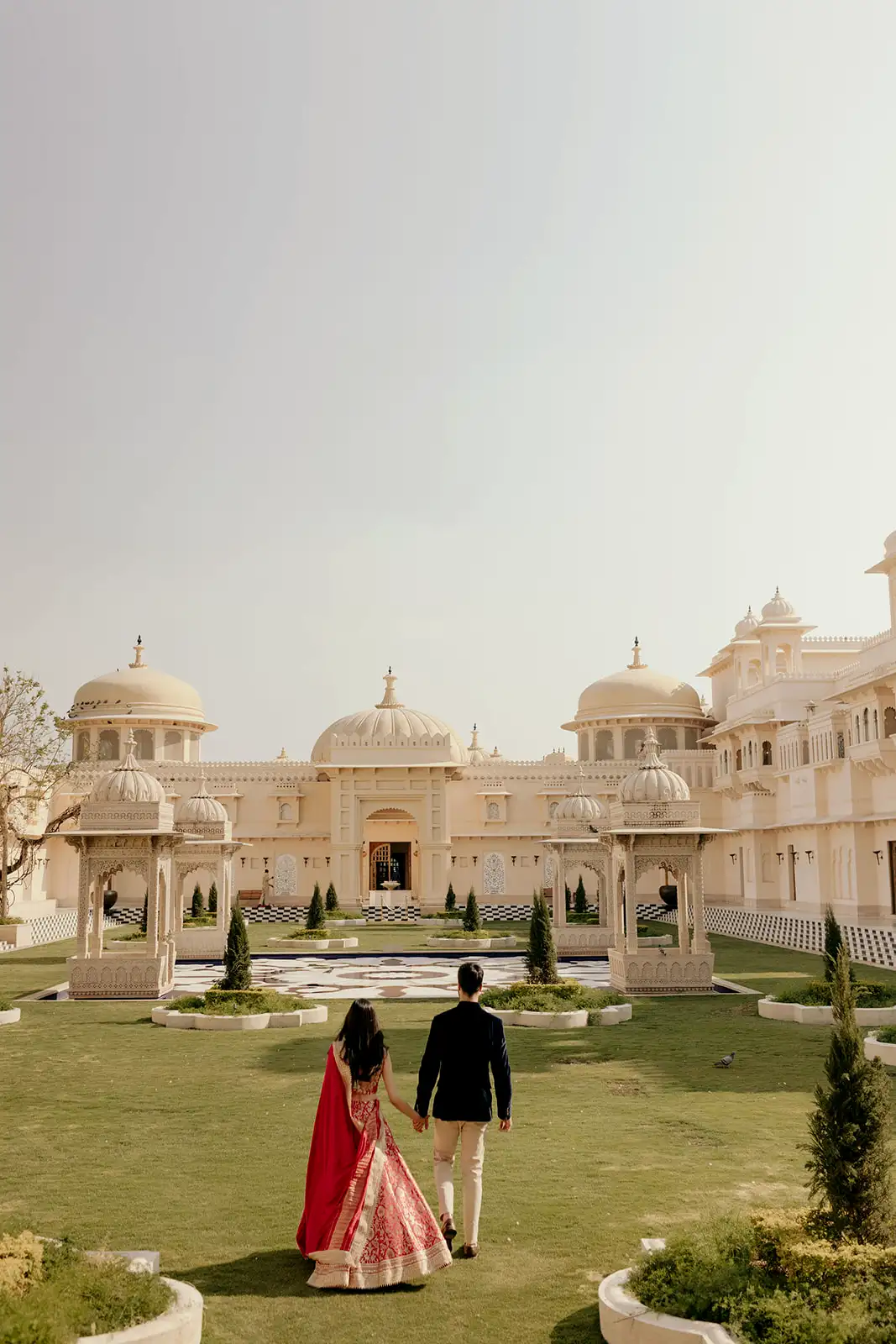 Couple holding hands while walking towards the domed palace courtyard at The Oberoi Udaivilas, Udaipur.