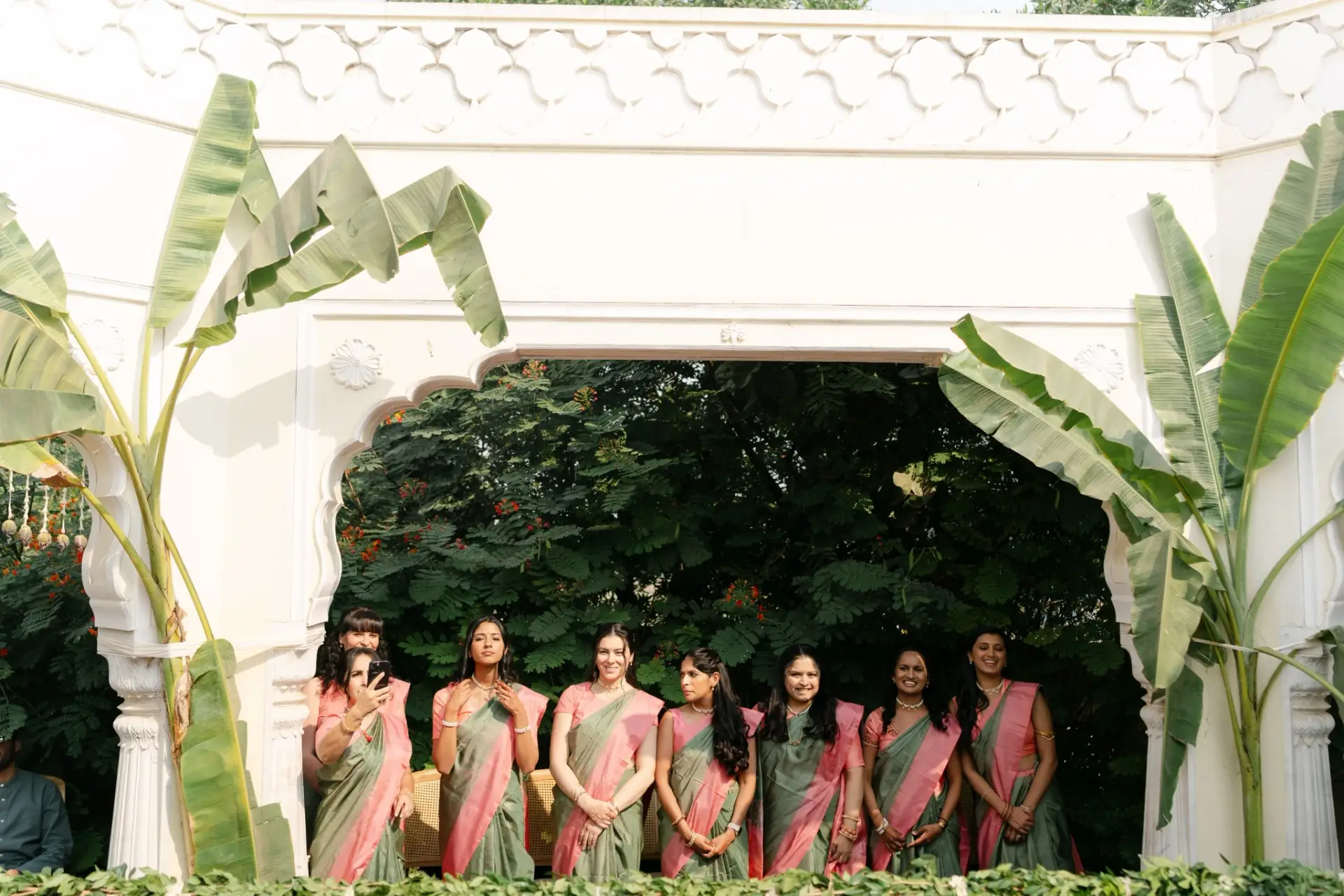 Bridesmaids in coordinated sarees beneath a leafy canopy at Hyatt Regency Jaipur Mansarovar, Jaipur