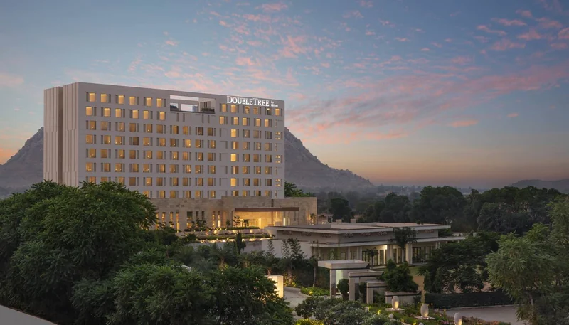 Exterior of DoubleTree by Hilton Jaipur Amer, with hotel signage and the Aravalli hills behind.