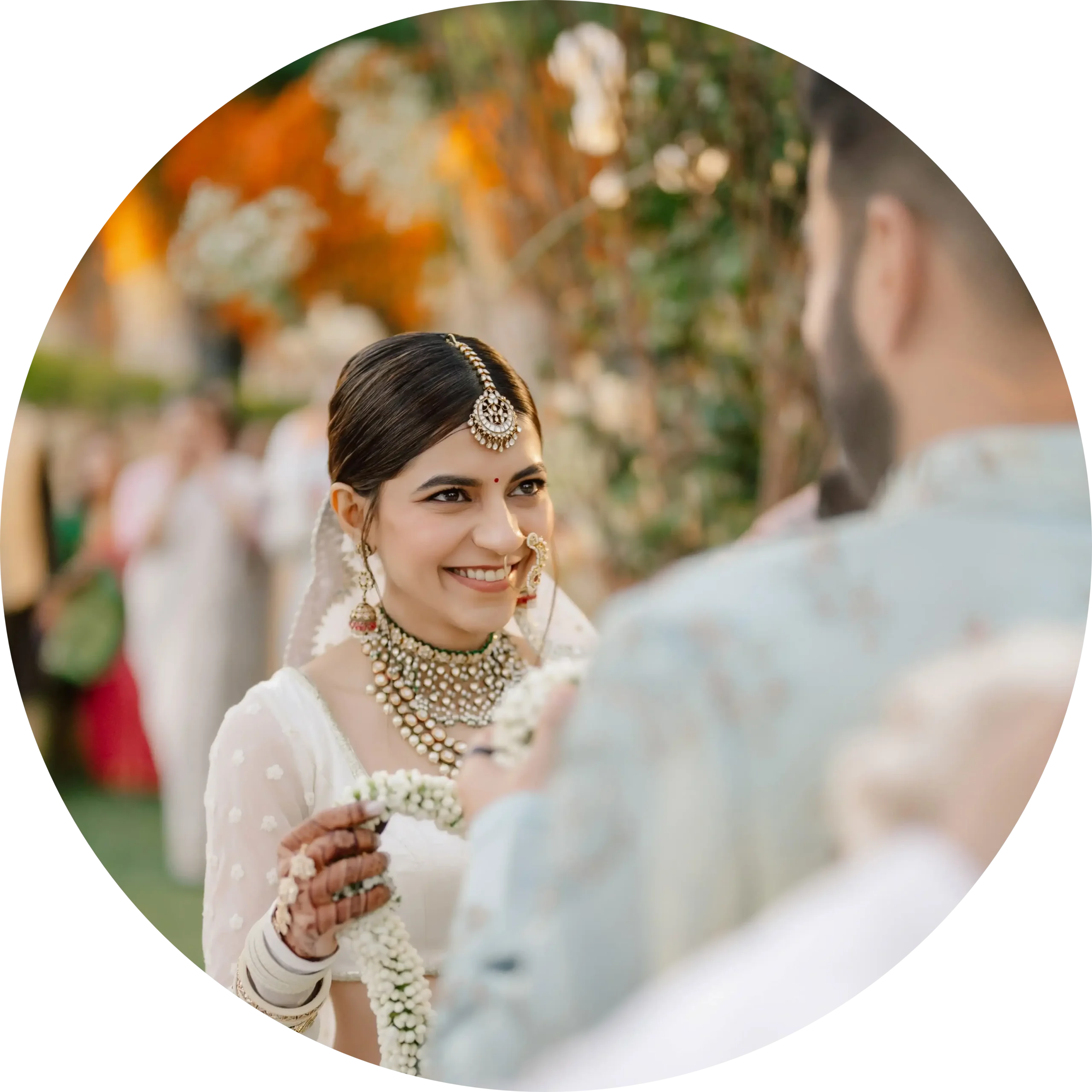 An Indian bride in white attire smiling warmly during a traditional outdoor varmala ceremony at Alila Fort Bishangarh in Jaipur, India.