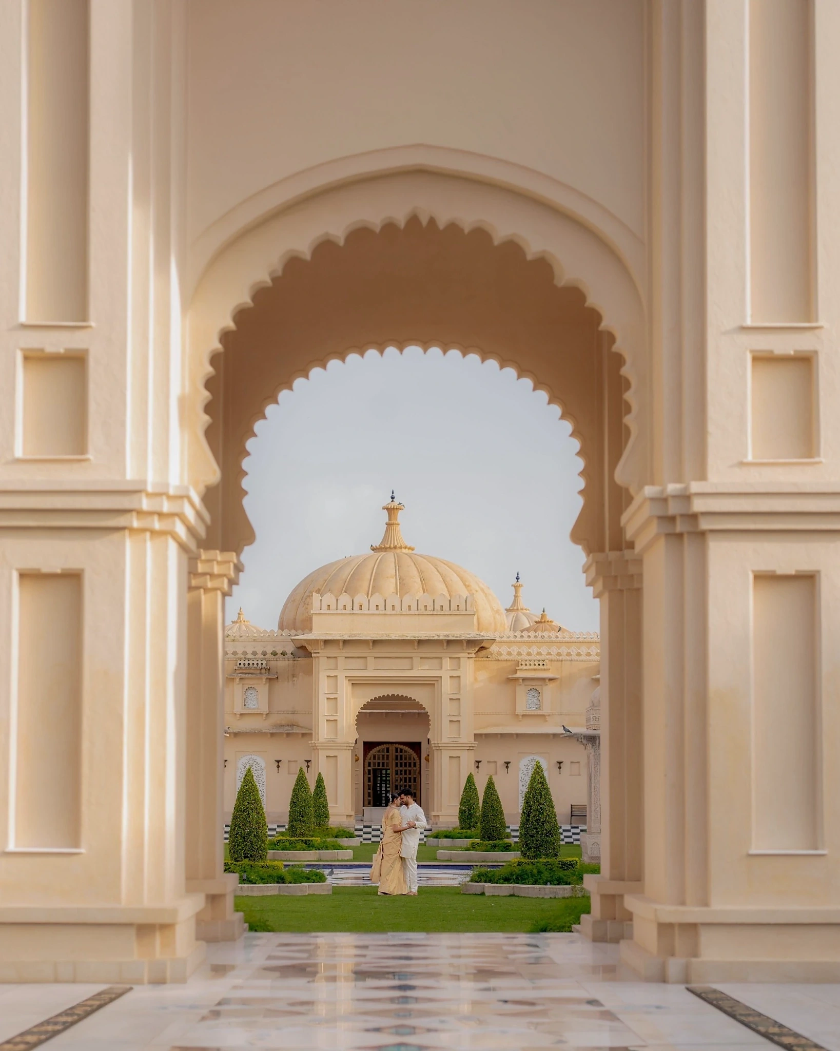 A couple stands in a courtyard at The Oberoi Udaivilas in Udaipur, framed by a scalloped arch, featured in the Indian wedding destinations gallery.